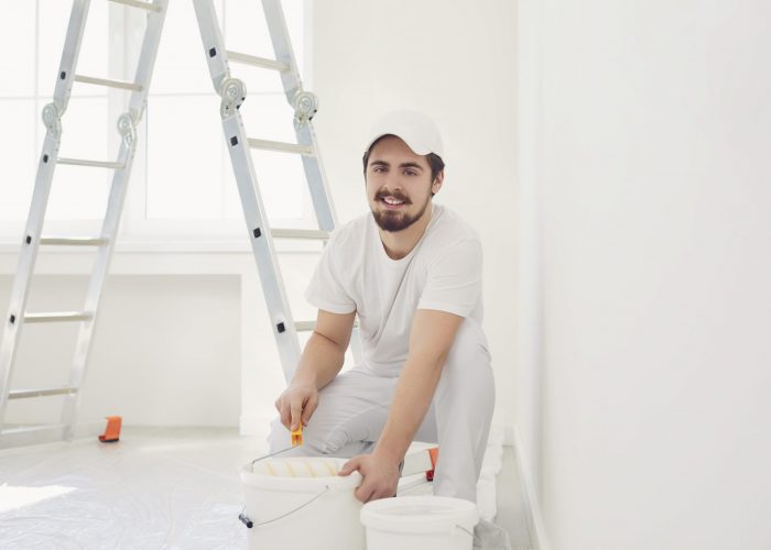 A male painter in a white uniform with a roller works in his hand in a white room.